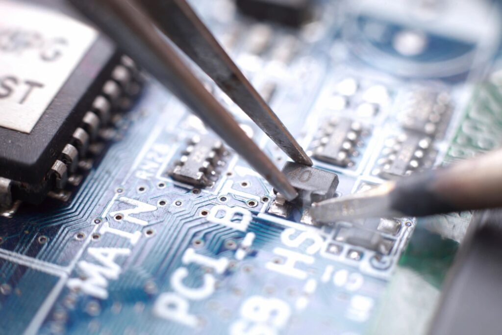 A person using tweezers on the top of a circuit board.